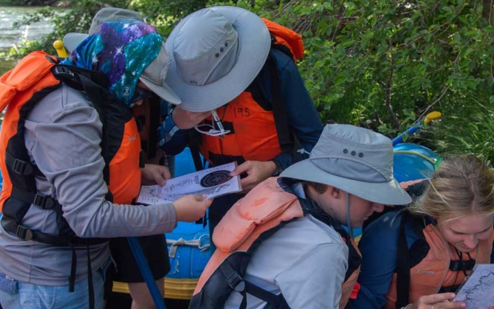 A group of people wearing sun hats and life jackets examine maps.
